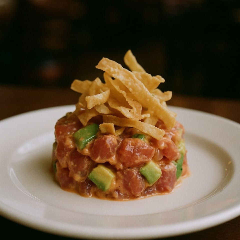 A tuna tartare with avocado cubes and crispy fried wonton strips on a white plate.